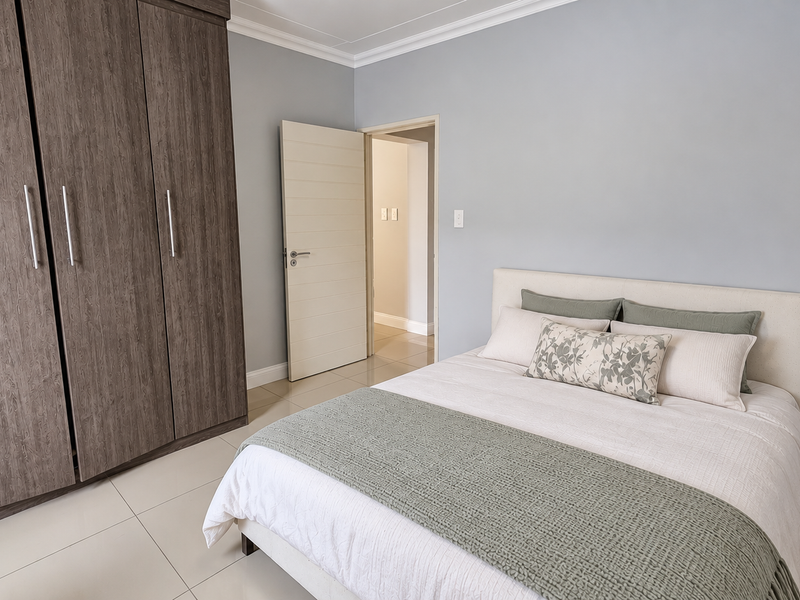 A well-maintained bedroom featuring neutral wall tones, large built-in cupboards with wood-grain finish, and light-colored floor tiles.