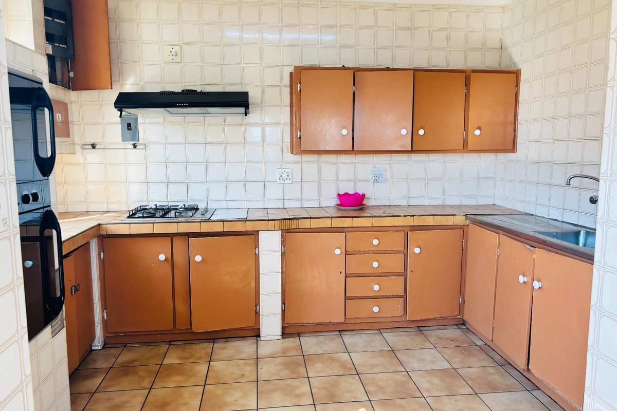 A functional kitchen featuring dated cabinetry, a gas hob with extractor fan, built-in oven, and tiled finishes throughout.