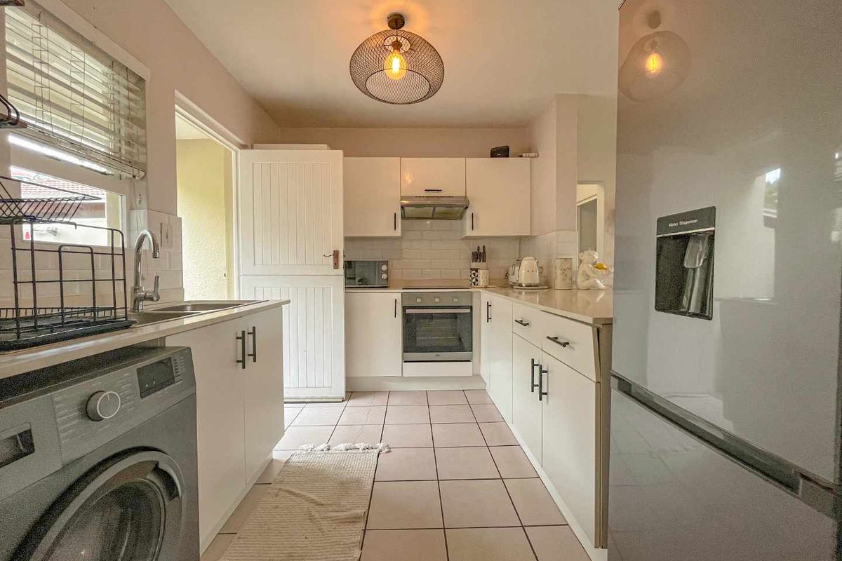 A functional kitchen featuring white cabinetry, tiled flooring, built-in oven, extractor fan, and integrated laundry plumbing.