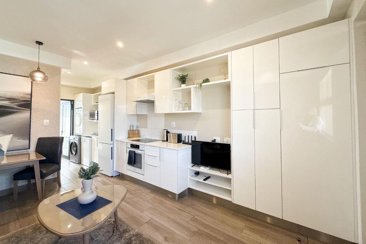 Modern open-plan living area featuring a sleek, high-gloss kitchen with integrated appliances, ample storage cabinetry, and durable tiled flooring throughout.