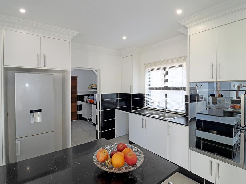 Modern kitchen featuring white cabinetry, black granite countertops, a double sink, and built-in oven, with an adjacent scullery area.