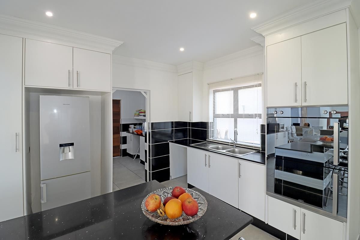 Modern kitchen featuring white cabinetry, black granite countertops, a double sink, and built-in oven, with an adjacent scullery area.