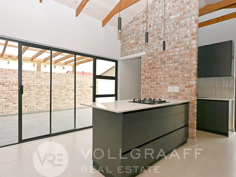 Modern kitchen featuring an exposed brick wall, timber ceiling beams, a central island with a gas hob, and large sliding doors leading to the patio.