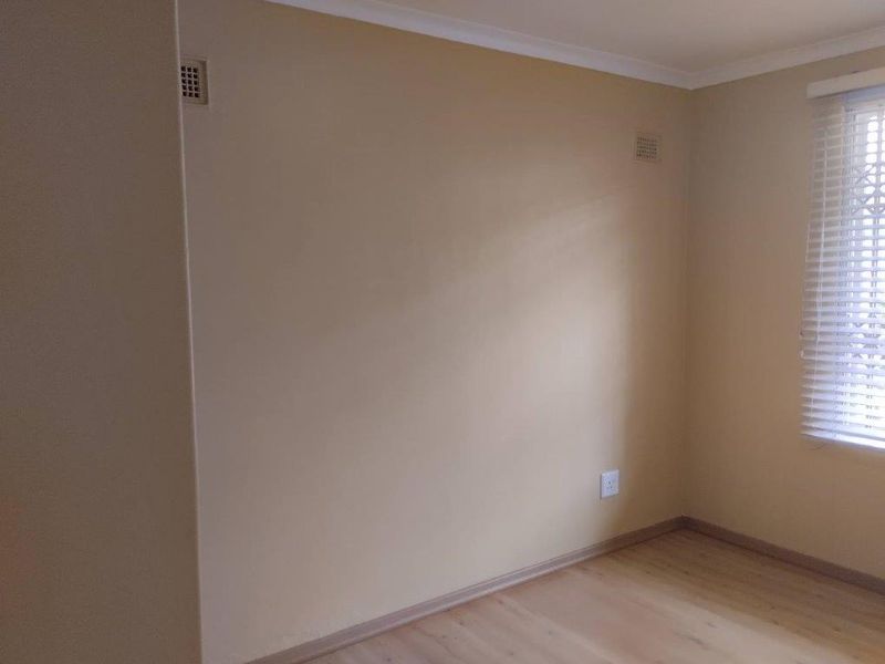 A clean, empty bedroom featuring light-toned laminate flooring, neutral walls, and fitted venetian blinds, offering a blank canvas for personalization.