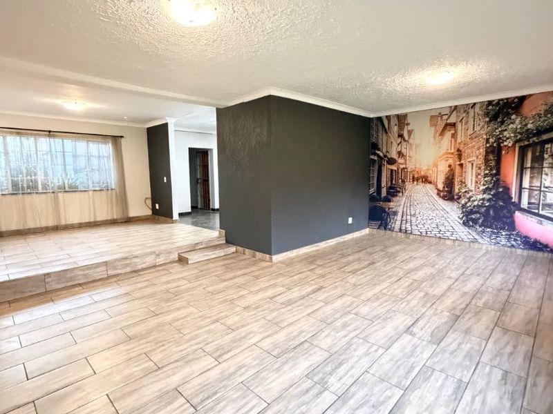 Spacious open-plan living area featuring wood-look tiled flooring, a raised platform section, and a prominent feature wall with a mural.