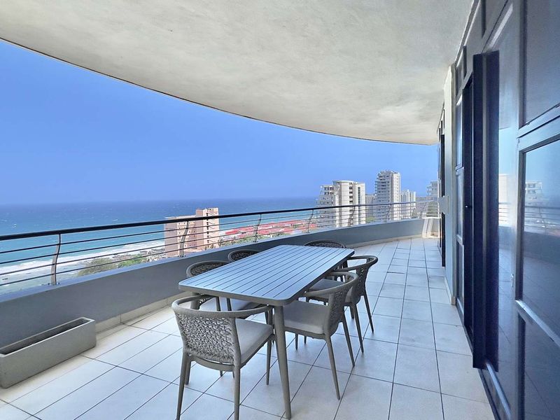 Spacious covered balcony featuring tiled flooring and metal railings, offering expansive ocean and city views.