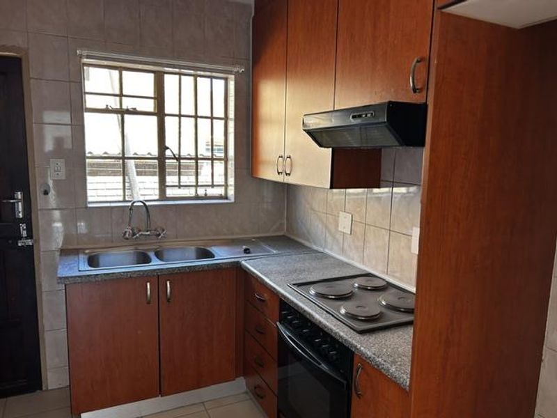 Compact kitchen featuring wood-look cabinetry, a double stainless steel sink, built-in oven with electric hob, and tiled splashbacks.