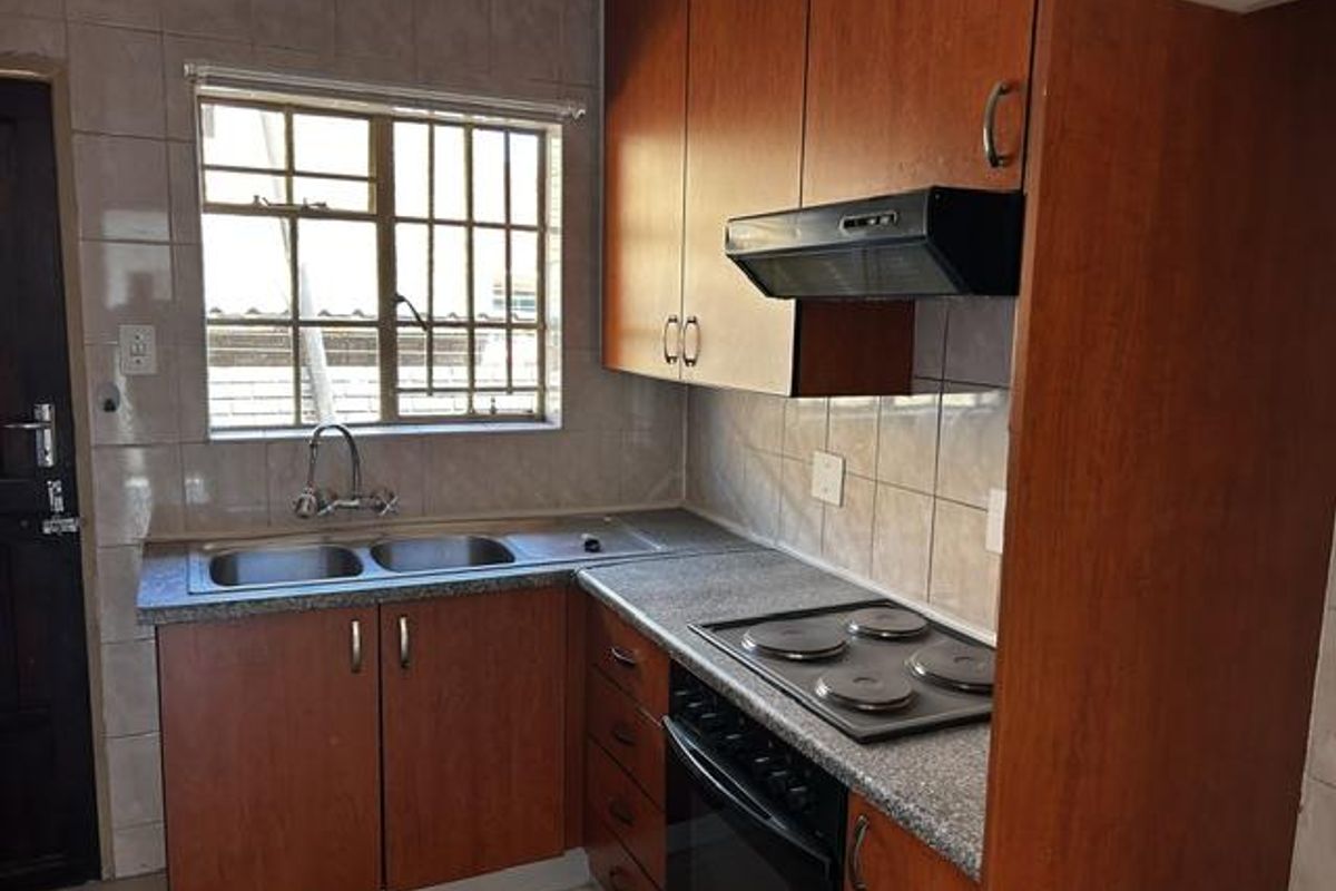 Compact kitchen featuring wood-look cabinetry, a double stainless steel sink, built-in oven with electric hob, and tiled splashbacks.