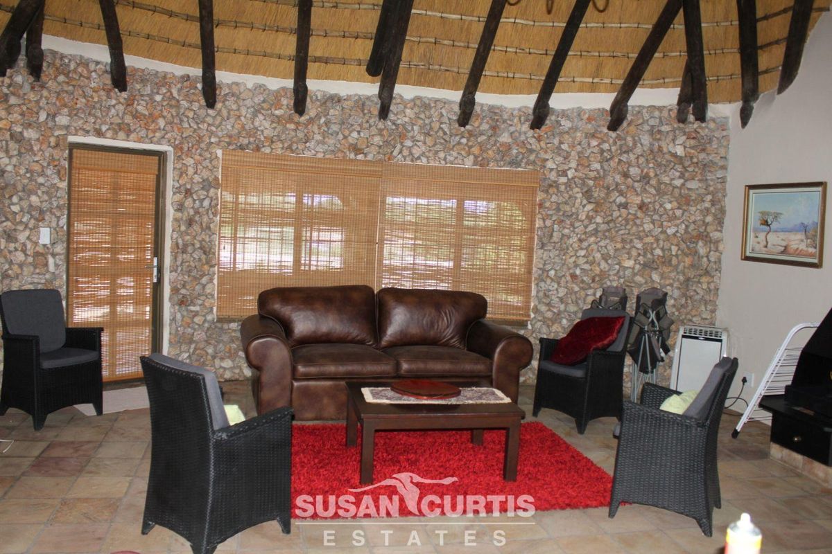 Spacious living area featuring a rustic stone feature wall, exposed timber beams, and a traditional thatched roof ceiling.