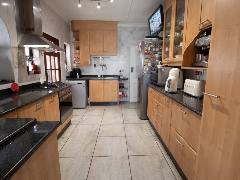 A functional kitchen featuring light wood cabinetry, dark granite countertops, a gas hob, and stainless steel extractor fan with neutral tiled flooring.