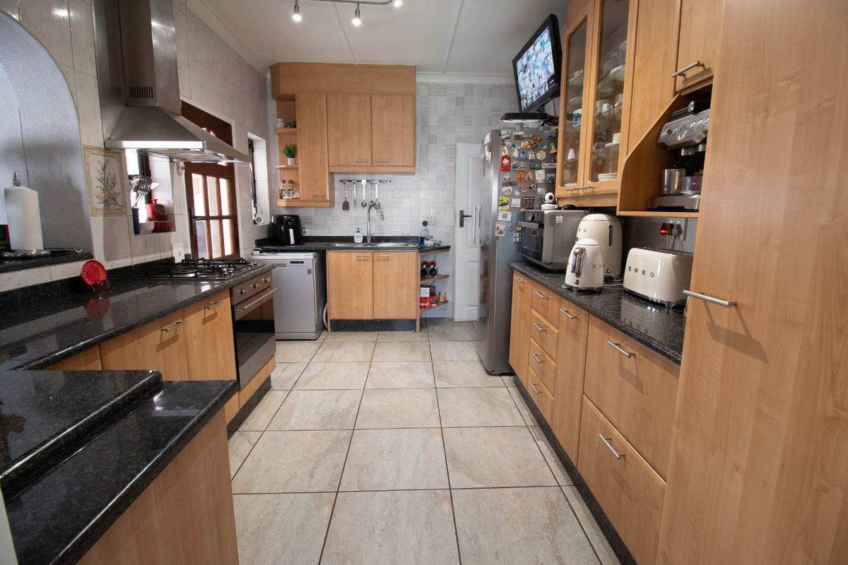 A functional kitchen featuring light wood cabinetry, dark granite countertops, a gas hob, and stainless steel extractor fan with neutral tiled flooring.