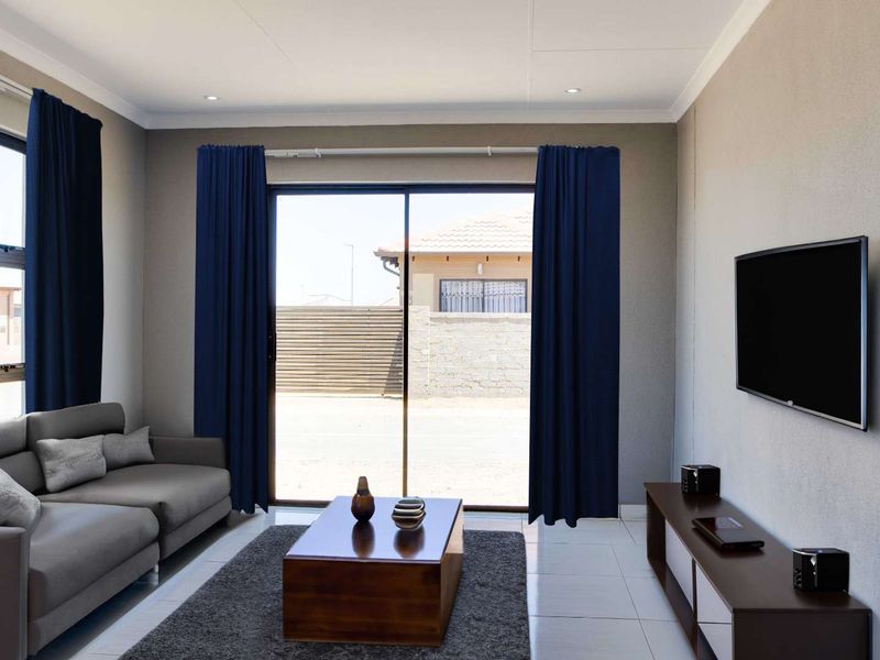 A modern living room featuring tiled flooring, recessed downlights, and a large sliding glass door providing natural light and access to the exterior.