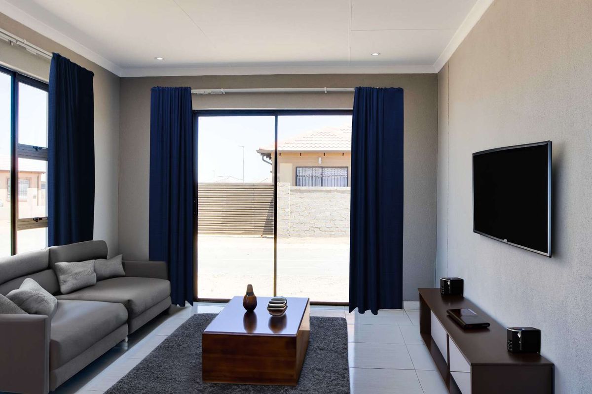 A modern living room featuring tiled flooring, recessed downlights, and a large sliding glass door providing natural light and access to the exterior.