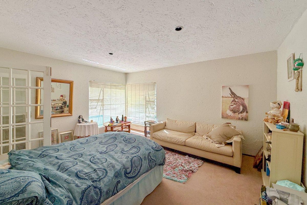 A spacious bedroom featuring neutral walls, carpeted flooring, and large windows with blinds, offering a comfortable and functional living space.