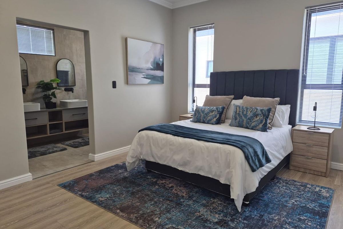 A modern, well-maintained bedroom featuring laminate flooring, crown molding, and an open-plan en-suite bathroom with a double vanity.