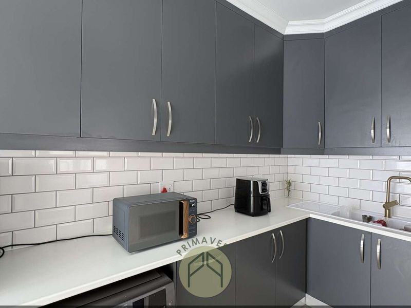 Modern kitchen featuring dark grey cabinetry, white subway tile backsplash, white countertops, and a brass faucet.
