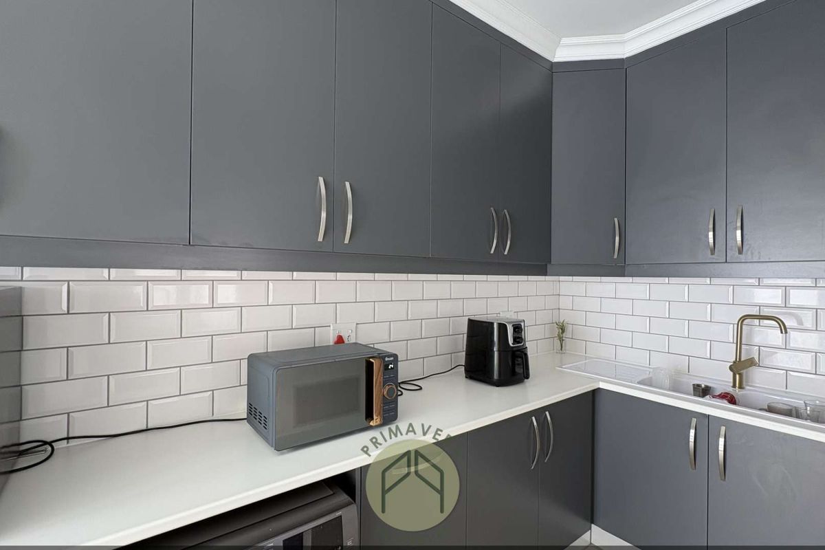 Modern kitchen featuring dark grey cabinetry, white subway tile backsplash, white countertops, and a brass faucet.