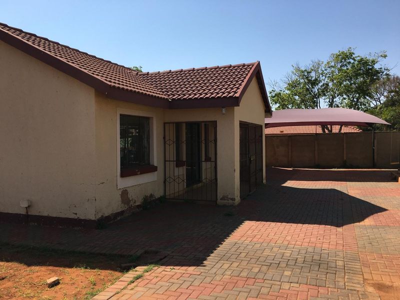 Front view of the property featuring a tiled roof, security gates, paved driveway, and a shade cloth carport within a walled perimeter.