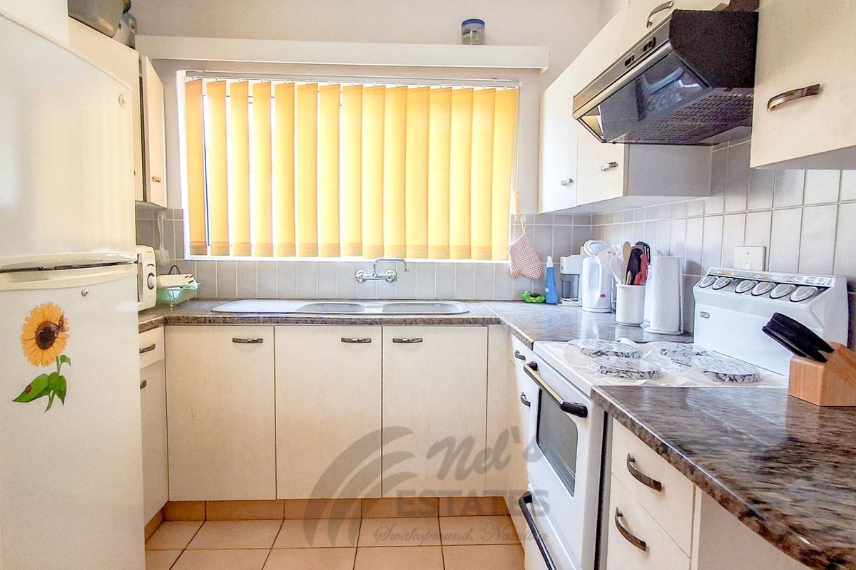 A functional kitchen featuring laminate countertops, double basin sink, tiled backsplash, and built-in cabinetry with an integrated extractor fan.
