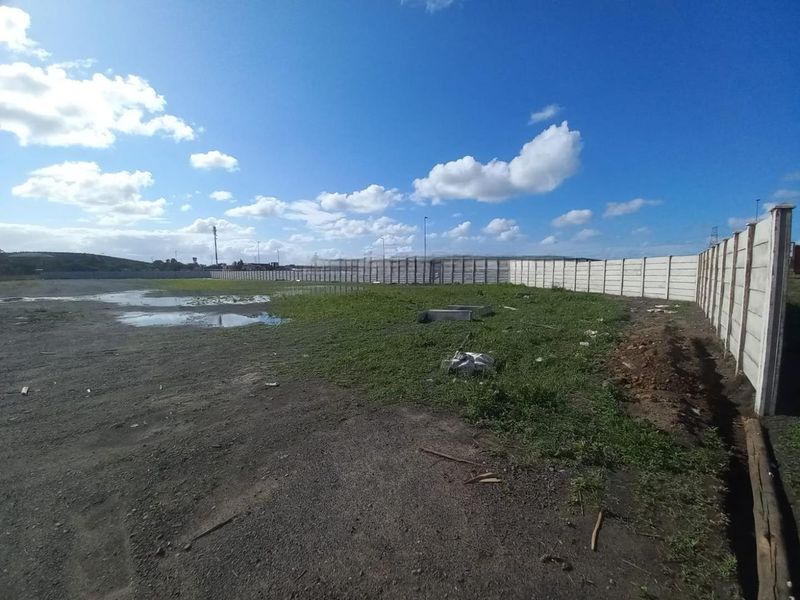 An expansive, unpaved industrial yard area enclosed by a precast concrete boundary wall, featuring uneven terrain and visible drainage issues.