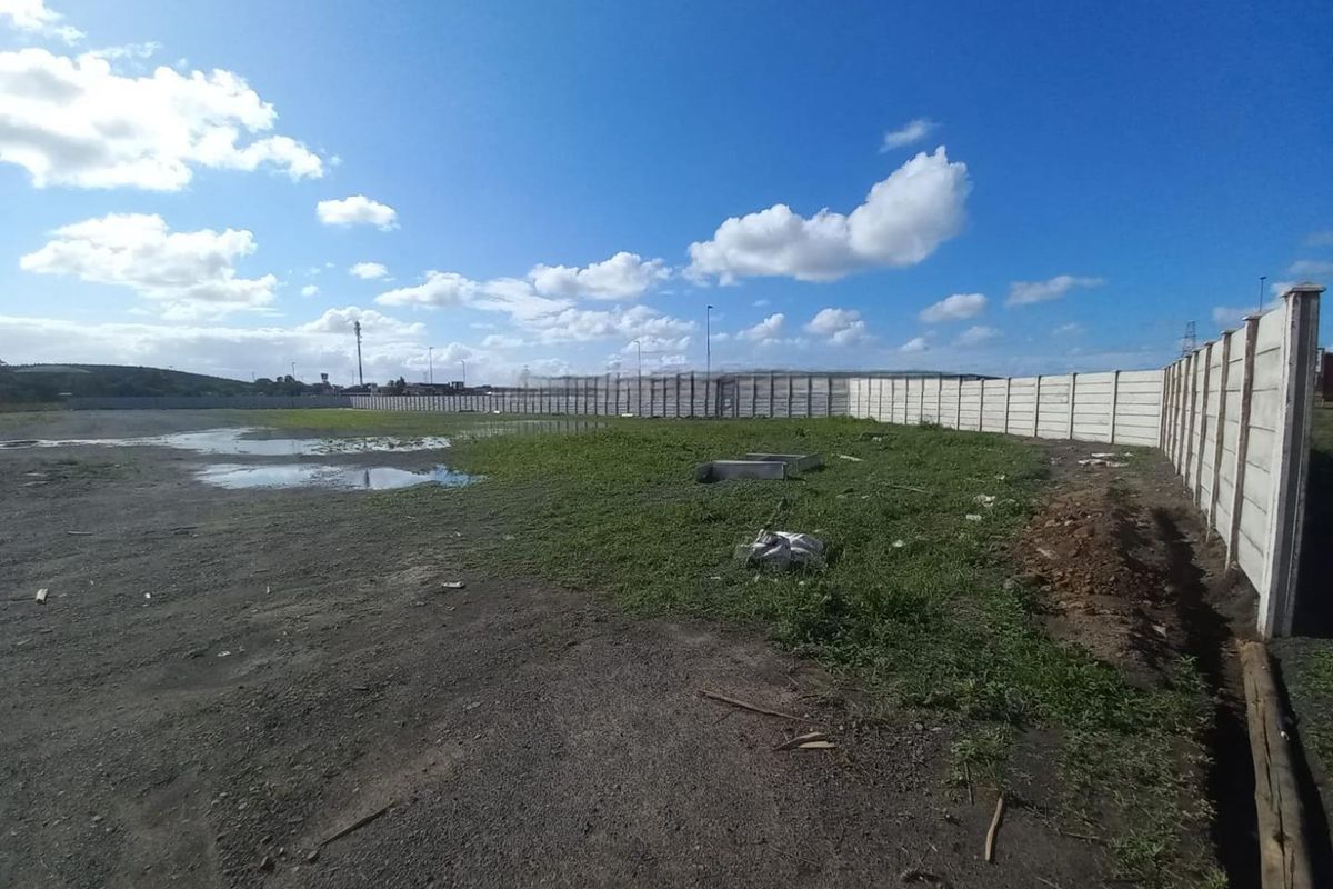An expansive, unpaved industrial yard area enclosed by a precast concrete boundary wall, featuring uneven terrain and visible drainage issues.