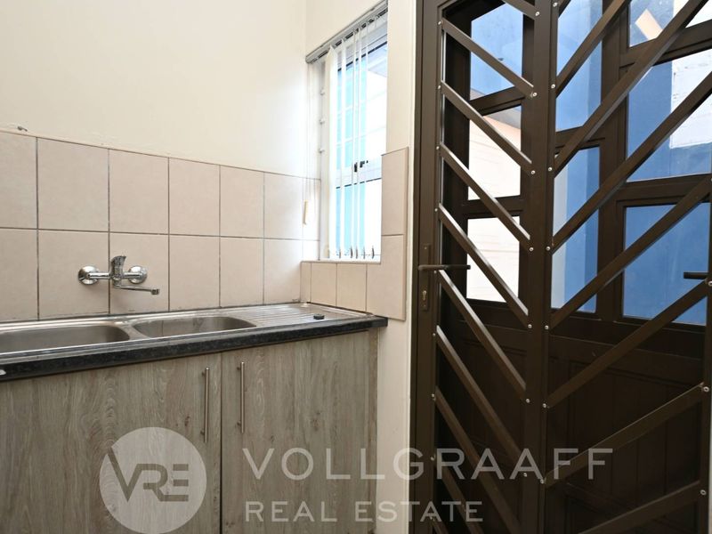 A functional laundry area featuring a stainless steel double sink, tiled splashback, laminate cabinetry, and a secure exterior access door.