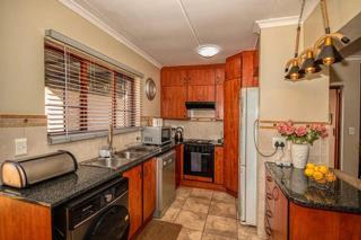 A functional kitchen featuring wooden cabinetry, granite countertops, built-in oven with extractor fan, and tiled flooring.