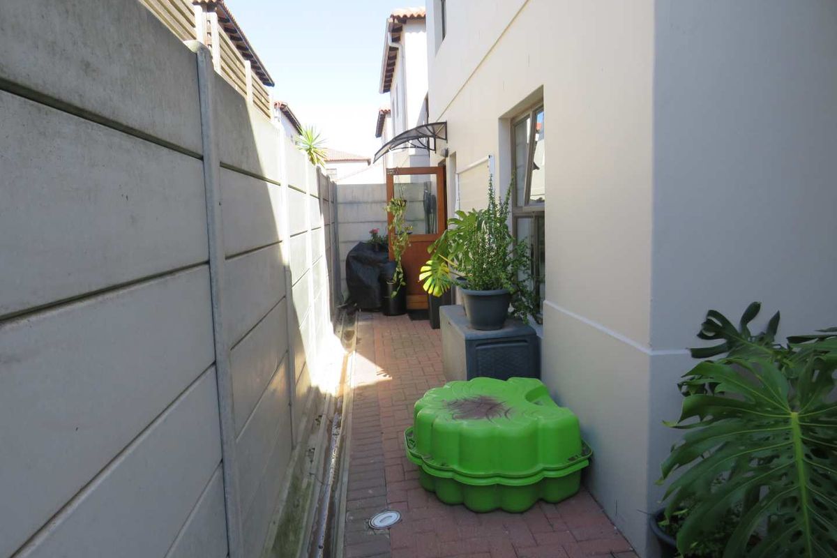A narrow side passage featuring a brick paved walkway, precast concrete boundary wall, and access to the rear of the property.