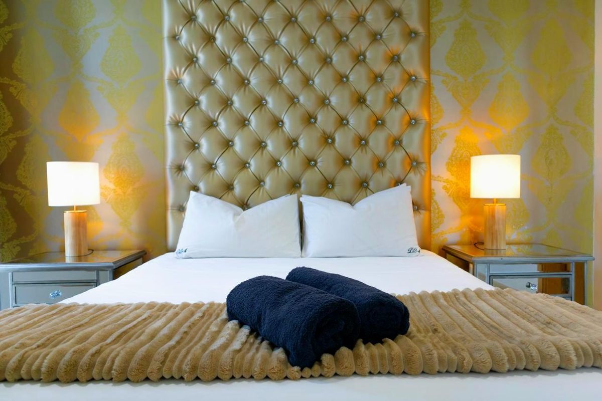 A well-appointed bedroom featuring a prominent tufted headboard and decorative wallpaper, creating a sophisticated and comfortable sleeping space.