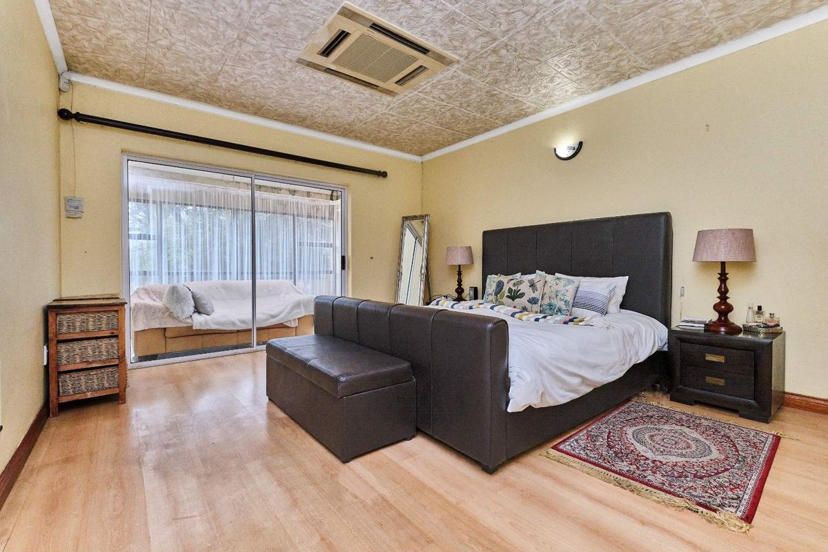 Spacious bedroom featuring laminate flooring, a textured ceiling with integrated air conditioning, and large sliding glass doors providing access to an outdoor area.