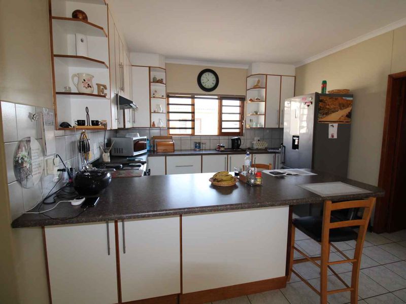 A functional kitchen featuring white cabinetry, laminate countertops, a tiled backsplash, and a breakfast bar area with tiled flooring.