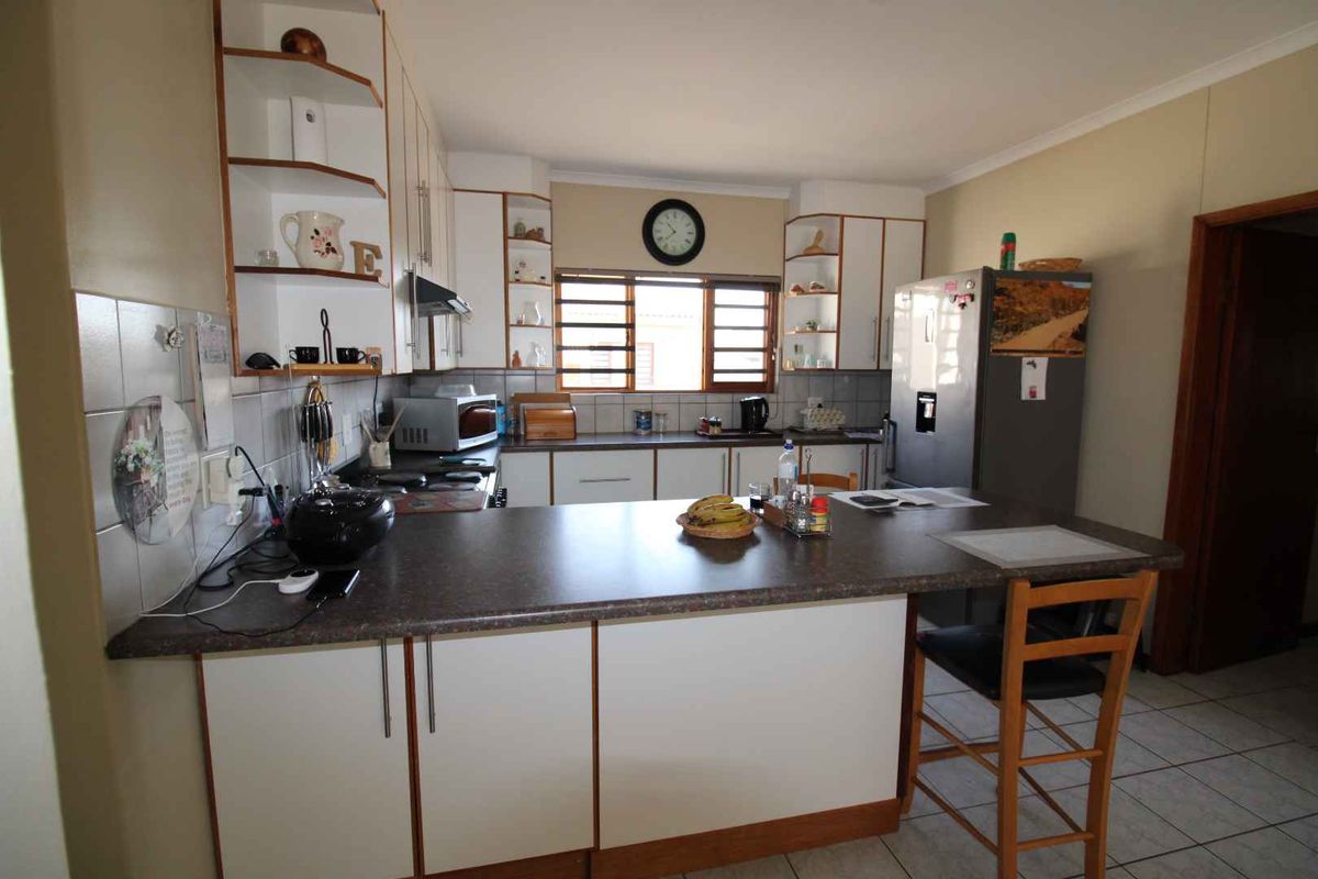 A functional kitchen featuring white cabinetry, laminate countertops, a tiled backsplash, and a breakfast bar area with tiled flooring.