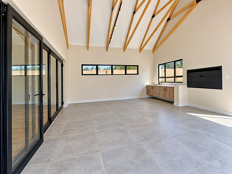 Spacious open-plan living area featuring a high vaulted ceiling with exposed timber trusses, tiled floors, built-in cabinetry, and large black aluminium sliding doors.