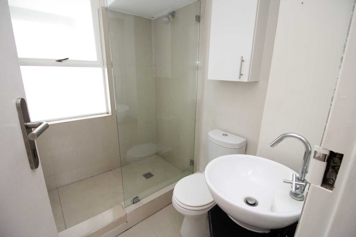 Compact bathroom featuring a glass-enclosed shower, modern vessel sink, and wall-mounted storage cabinet with neutral tile finishes.