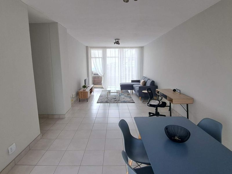 Spacious open-plan living and dining area featuring neutral tiled flooring and large sliding glass doors leading to a balcony, providing ample natural light.