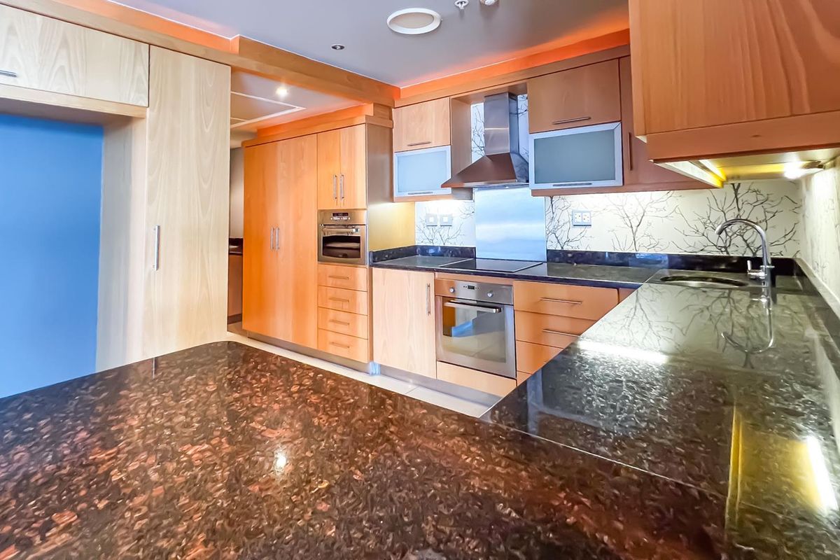 A functional kitchen featuring light wood cabinetry, dark granite countertops, integrated oven, hob, and extractor fan with modern recessed lighting.