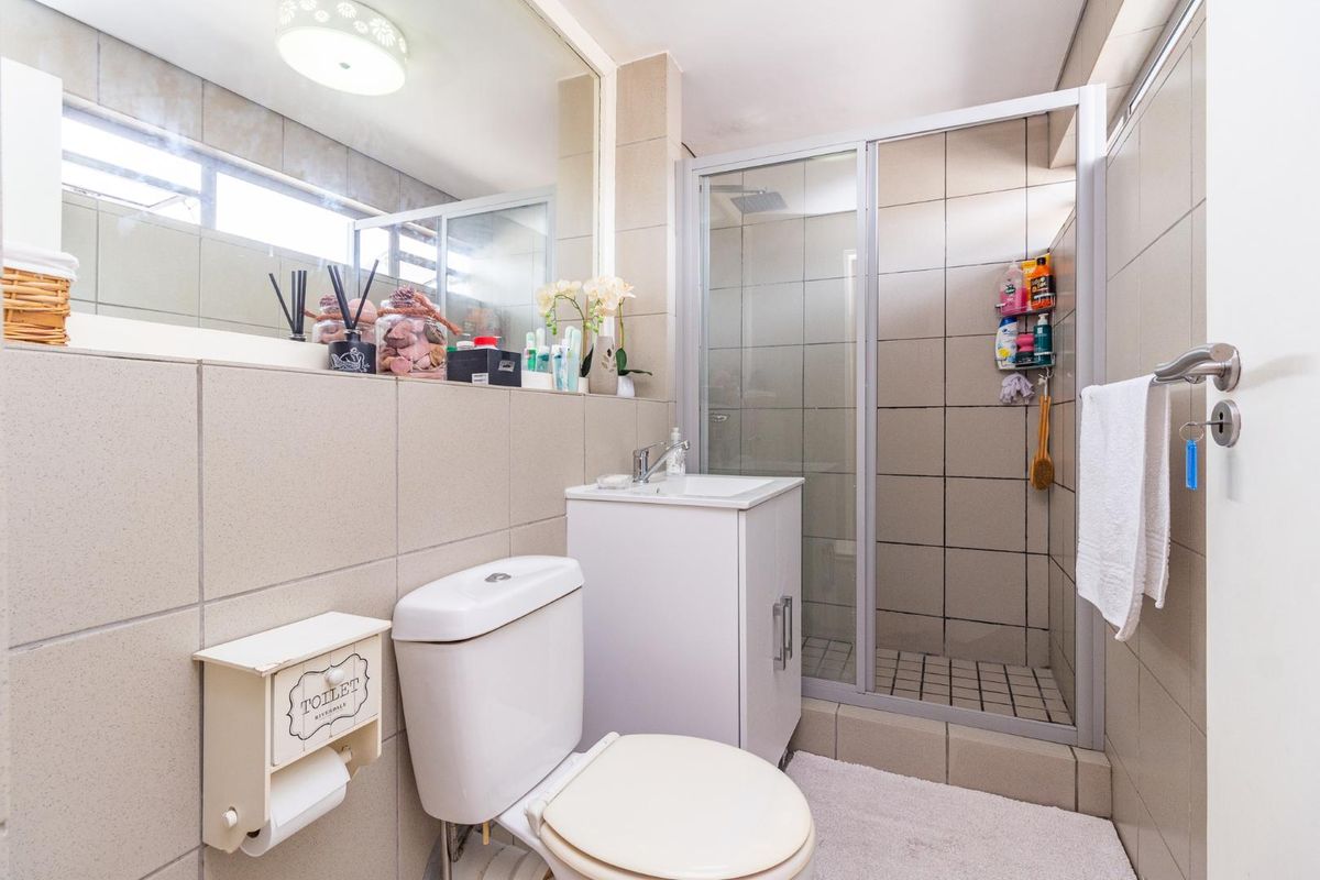 A functional bathroom featuring a shower enclosure, vanity basin, and toilet with neutral wall tiling and a large mirror.