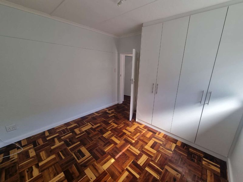 A bright, empty bedroom featuring polished parquet flooring and ample built-in cupboard storage space.