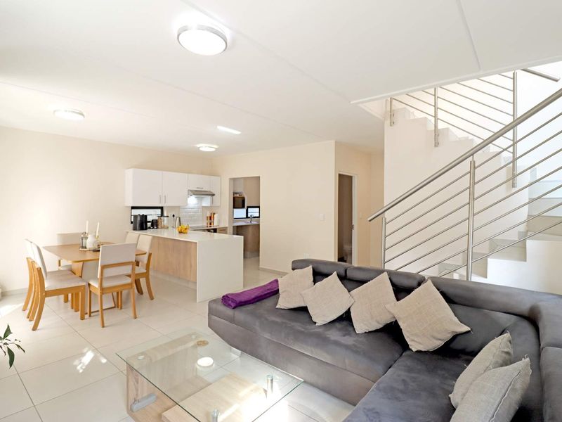 Spacious open-plan living and dining area featuring a modern kitchen with island, tiled floors, and a staircase with stainless steel balustrade.