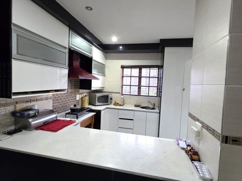 Modern kitchen featuring high-gloss cabinetry, stone countertops, a tiled backsplash, and integrated extractor fan, offering a clean and functional workspace.