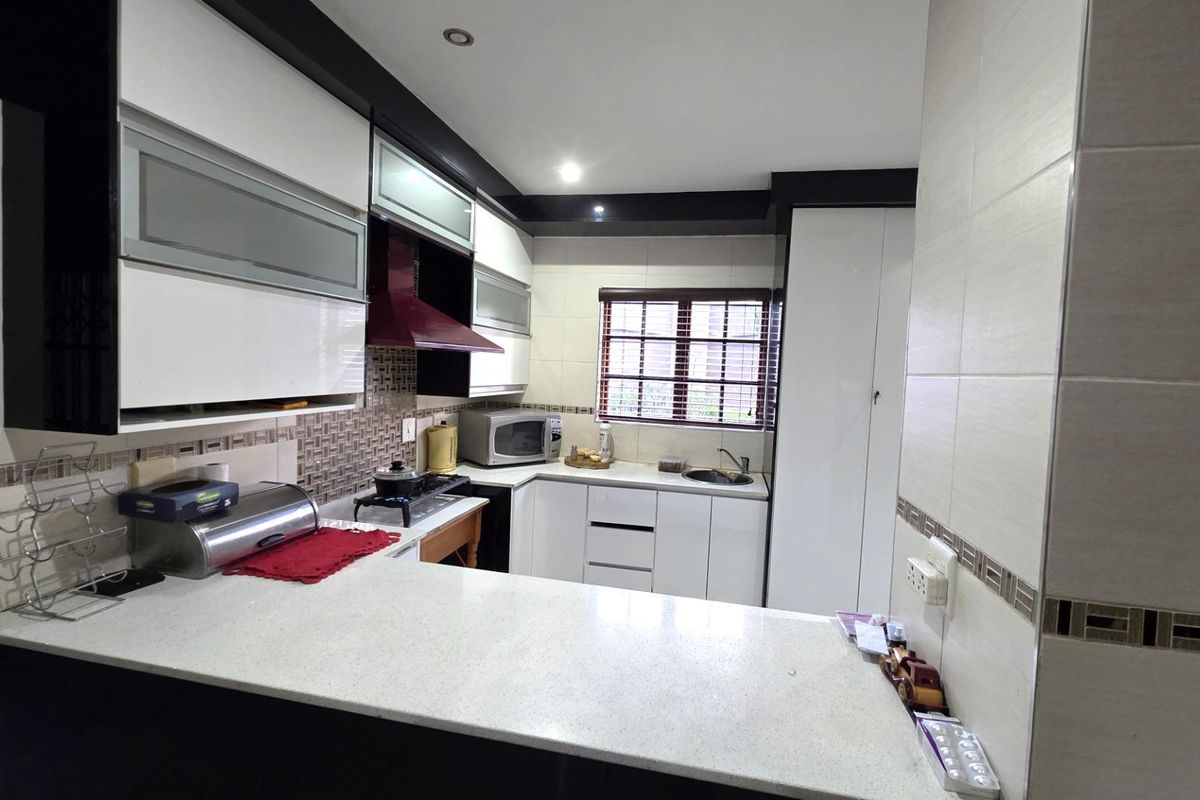 Modern kitchen featuring high-gloss cabinetry, stone countertops, a tiled backsplash, and integrated extractor fan, offering a clean and functional workspace.