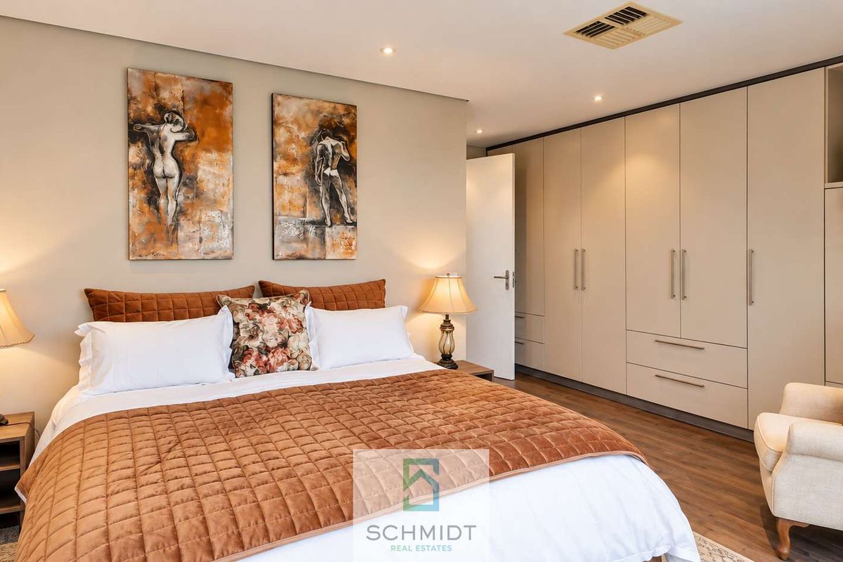 A well-appointed bedroom featuring extensive built-in cabinetry, recessed ceiling lighting, and modern laminate flooring, creating a clean and functional living space.