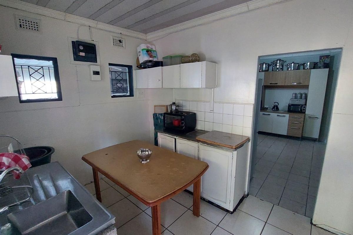 A functional kitchen area featuring built-in cabinetry, tiled splashbacks, and a stainless steel sink, with an adjacent scullery or secondary prep area visible.