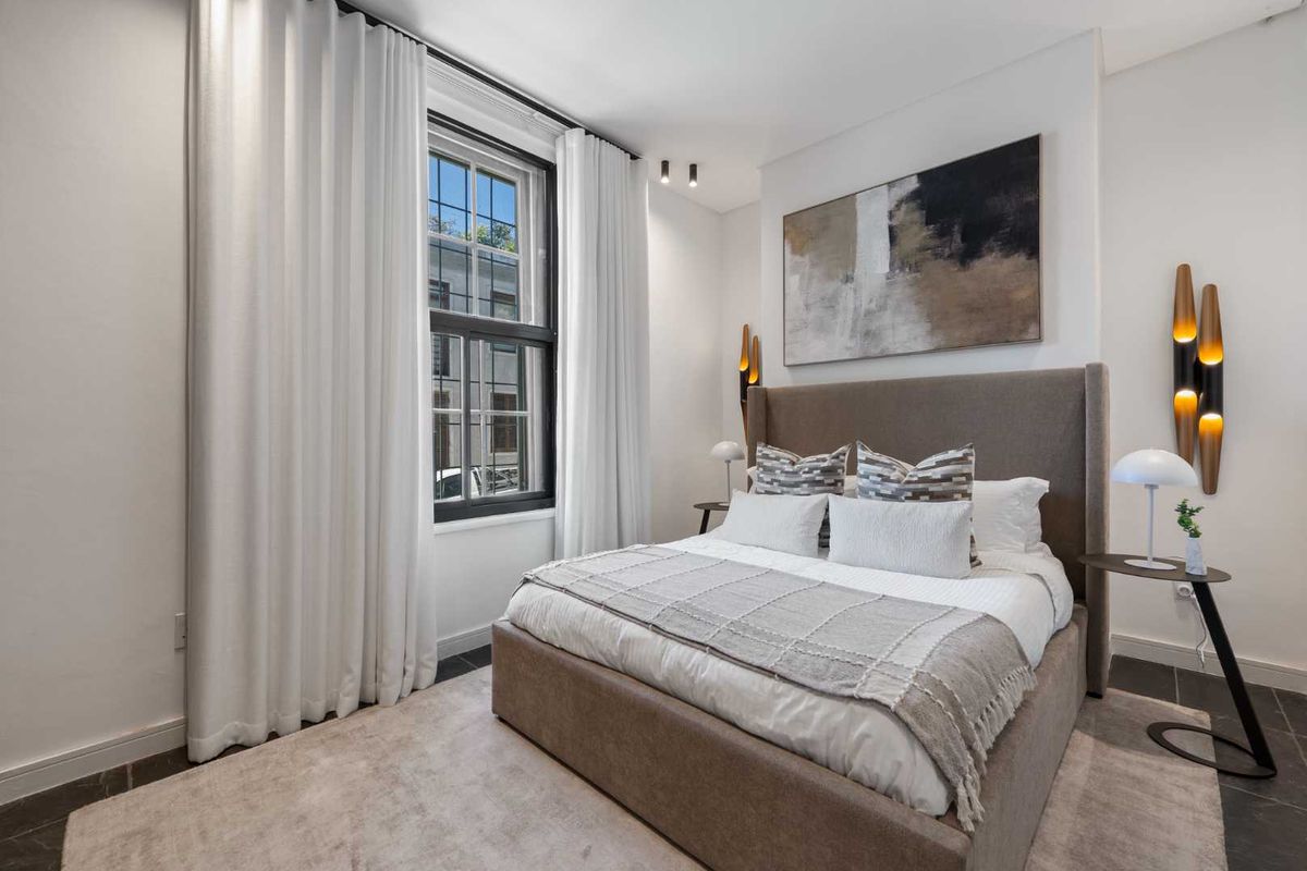 A well-appointed bedroom featuring dark tiled flooring, a large sash window with floor-to-ceiling curtains, and modern recessed ceiling lighting.
