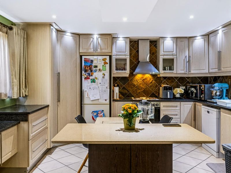 A functional kitchen featuring light wood cabinetry, granite countertops, a tiled backsplash, and a central island, illuminated by recessed downlights.