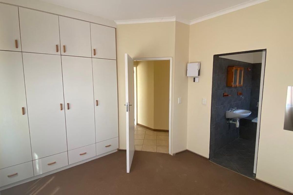 A bedroom featuring extensive built-in cabinetry and an en-suite bathroom with tiled finishes and a wall-mounted basin.