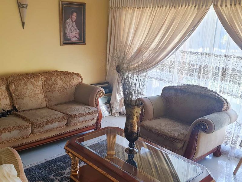 A comfortable living room featuring tiled flooring, neutral wall tones, and large windows dressed with layered curtains.