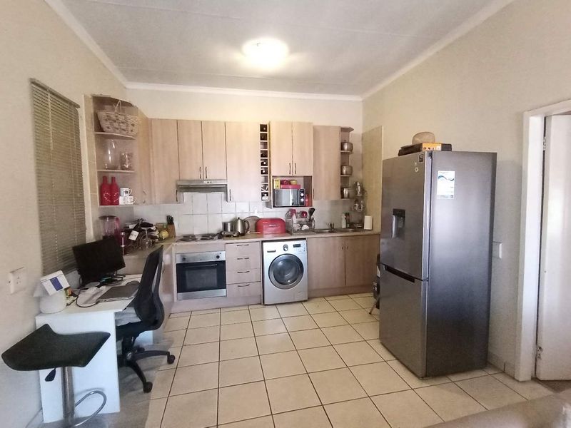 Functional kitchen featuring light wood-finish cabinetry, built-in oven, hob, extractor fan, and integrated washing machine with tiled flooring throughout.