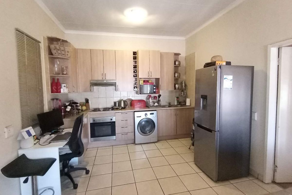 Functional kitchen featuring light wood-finish cabinetry, built-in oven, hob, extractor fan, and integrated washing machine with tiled flooring throughout.