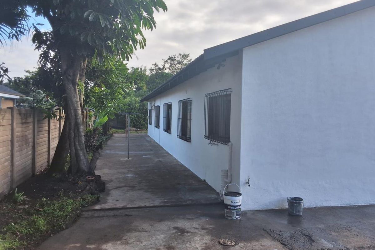 A view of the rear exterior of the house featuring a concrete pathway, security bars on windows, and a boundary wall.